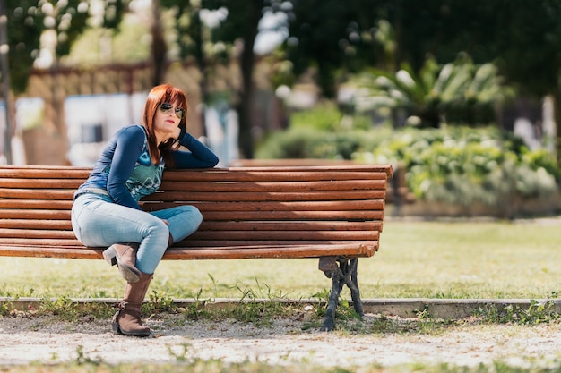 Foto mulher contemplando seus arredores. sentado em um banco de parque em um dia ensolarado