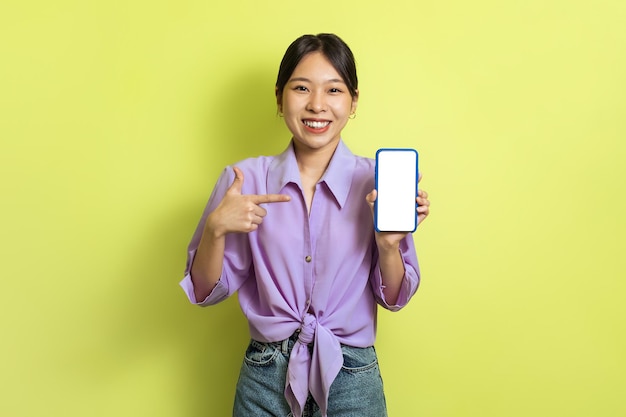 Mulher coreana feliz mostrando a tela em branco do telefone sobre fundo amarelo