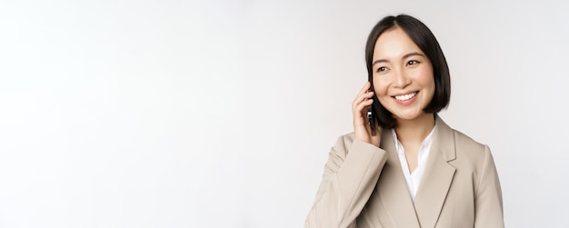 Mulher corporativa sorridente de terno falando no celular tendo uma chamada de negócios no smartphone em pé sobre fundo branco