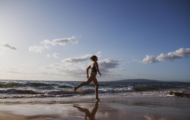 Mulher corre na praia, garota esportiva correndo à beira-mar na praia tropical durante as férias e