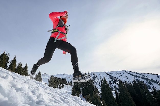 Mulher corredora de trilha correndo nas montanhas de inverno na neve Dinâmica correndo ladeira abaixo na trilha mulher atleta corredor vista lateral