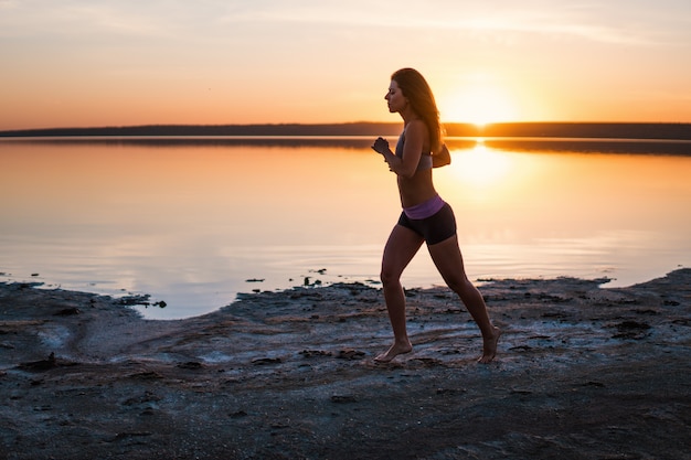 Mulher correndo na praia ao pôr do sol.