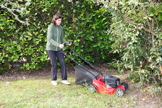 Mulher corta a grama entre as árvores em seu jardim