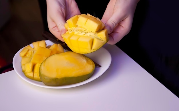 Mulher corta a manga em cubos para a polpa da fruta, separando-se facilmente da casca com uma faca de cozinha