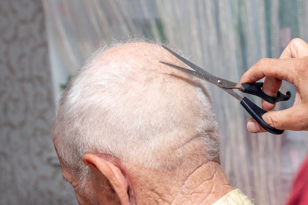 Mulher corta o cabelo de um homem idoso em casa Closeup