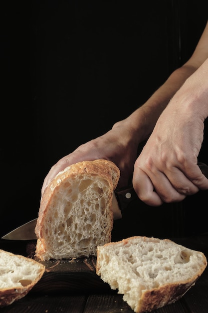 Mulher corta pão fresco com uma faca na mesa closeup Pão artesanal fresco no quadro vertical da mesa da cozinha Comida saudável e conceito de padaria tradicional