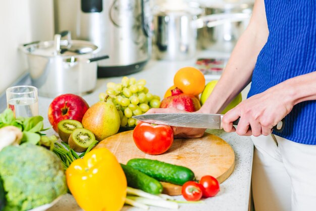 Mulher corta tomate pela faca na tábua de madeira na cozinha