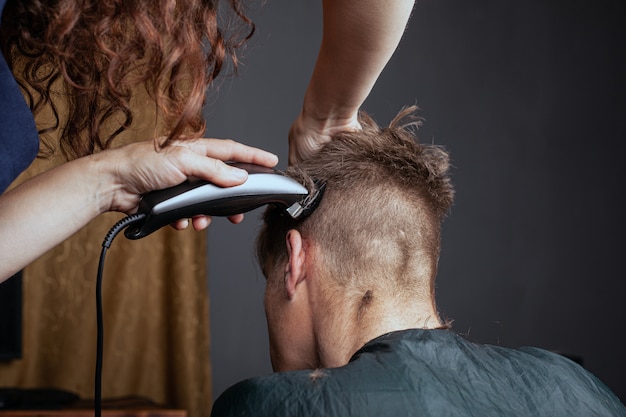 Mulher corta um homem com um aparador de cabeleireiro. corte de cabelo à moda.