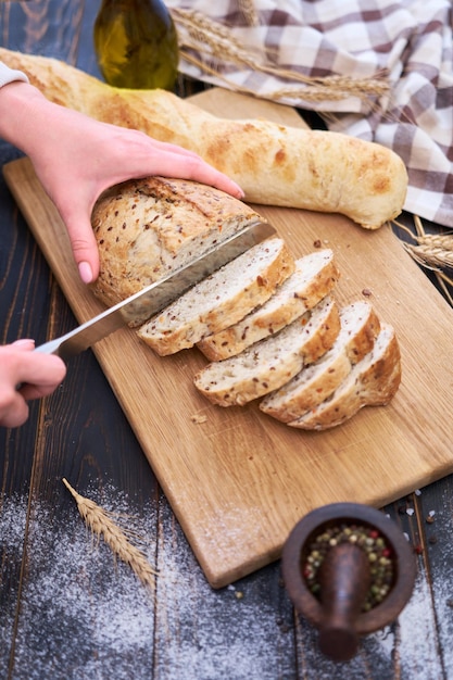 Mulher cortando pão fresco na mesa de cozinha de madeira