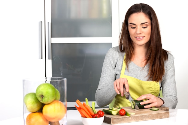 Foto mulher cortando pepino e vegetais na cozinha