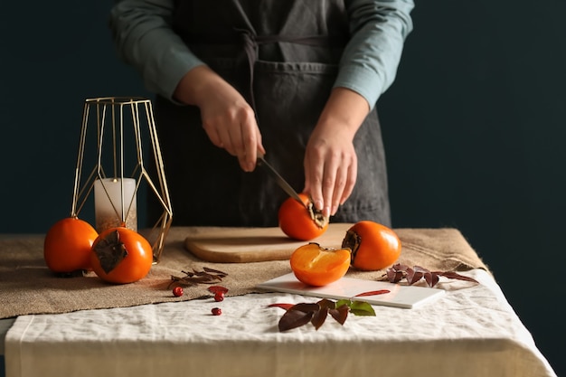 Mulher cortando saborosa fruta de caqui na mesa