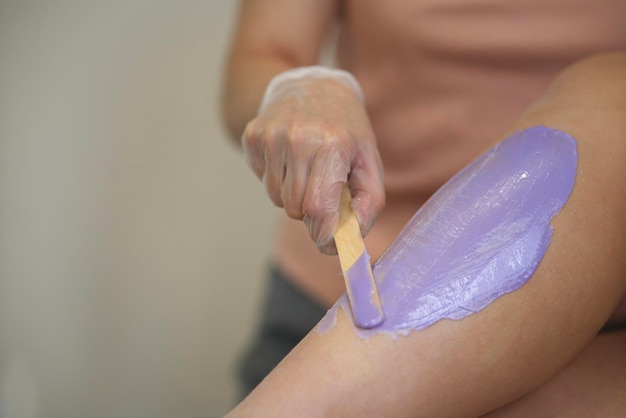 Mulher cosmetologista aplicando cera na perna de uma jovem antes do procedimento de depilação ou depilação. Menina deitada em um sofá em um salão de beleza, durante o procedimento de shugaring