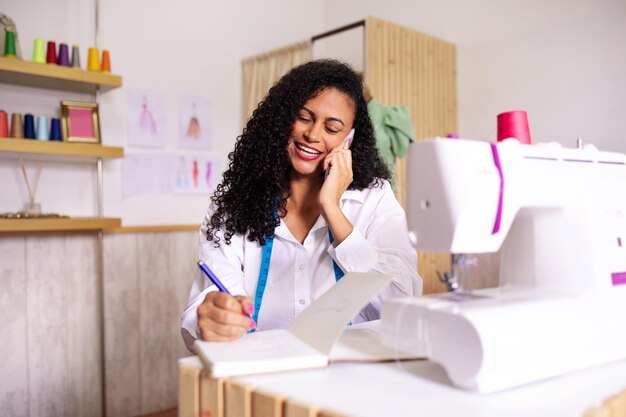 Foto mulher costureira conversando no telefone fazendo anotações no ateliê moderno