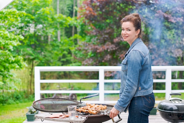 Mulher cozinha churrasco para sua família no jardim de uma casa de campo usando