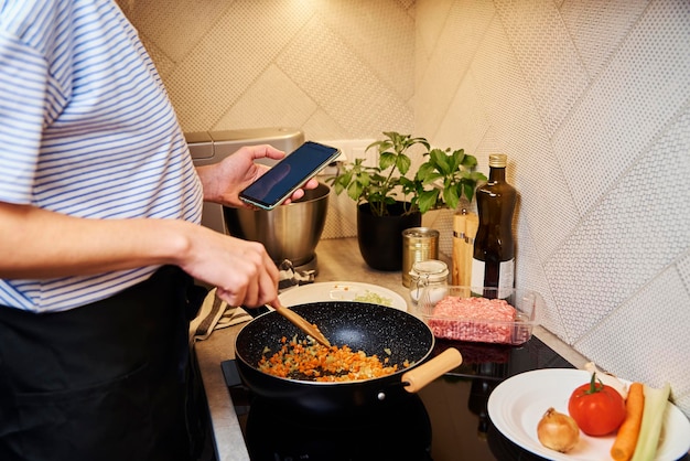 Mulher cozinhando molho à bolonhesa e usa smartphone