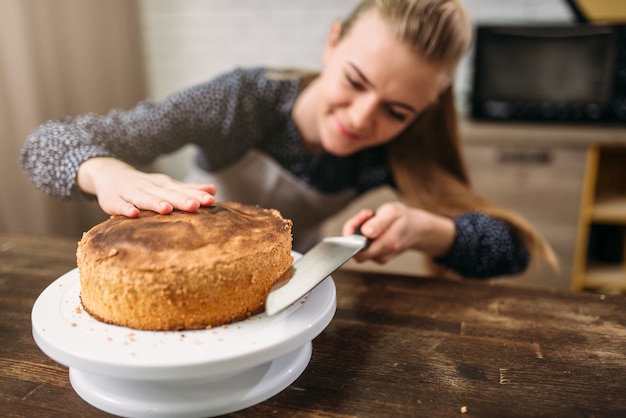 Mulher cozinheira corta bolo fresco com uma faca.