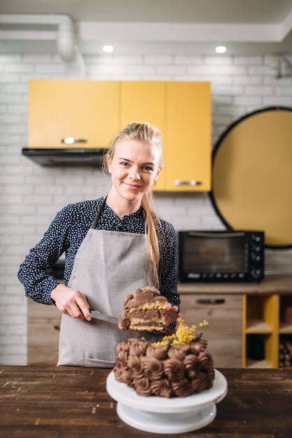 Mulher cozinheira segurando um pedaço de bolo de chocolate na lâmina