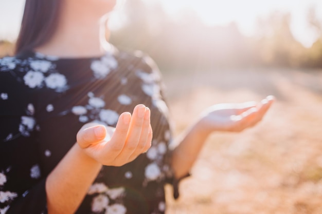 Mulher crente religiosa orando, levantando as mãos para receber o espírito de Deus, no campo ao pôr do sol.