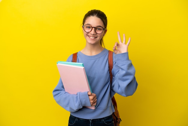 Mulher criança estudante sobre fundo amarelo isolado mostrando sinal de ok com os dedos