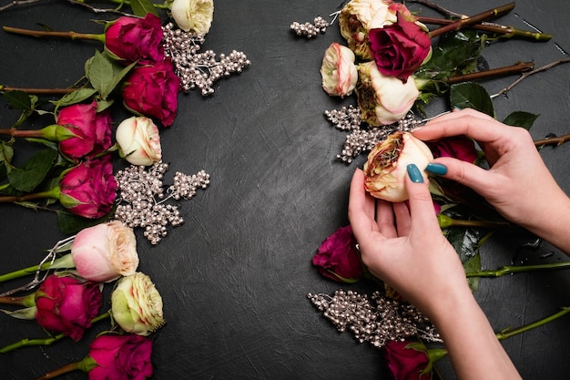 Mulher criando uma composição de buquê de rosas vermelhas e cor de rosa em fundo escuro. Arte de floricultura e arranjos florais. Belo conceito de design