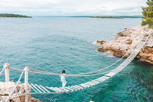 Mulher cruzando o mar da ponte suspensa no horário de verão de fundo