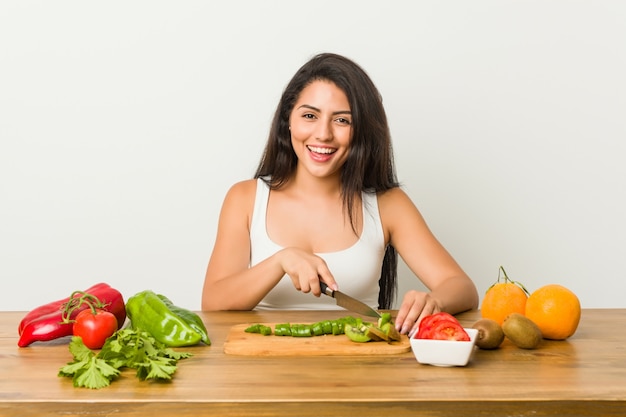 Mulher curvilínea nova que prepara uma refeição saudável feliz, sorridente e alegre.