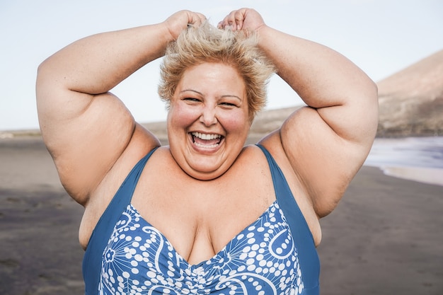 Mulher curvilínea sorrindo para a câmera usando biquíni e praia ao fundo