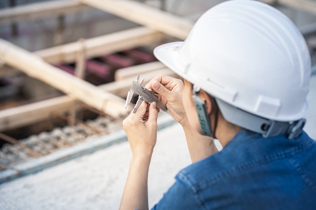 Foto mulher da engenharia que guarda o compasso de calibre vernier para medir um objeto no canteiro de obras. trabalhador está ajustando a pinça vernier.