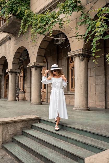 Mulher da menina da moda olhando a cidade velha. garota na europa. conceito de viagens. linda garota com vestido branco e chapéu. modelo de moda no fundo da rua. estilo de vida, viagens, férias, turismo