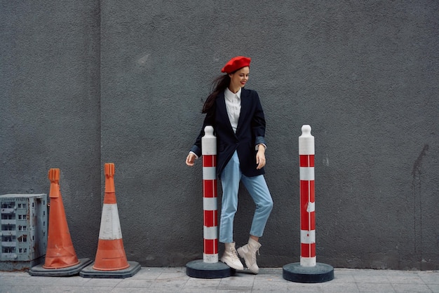 Mulher da moda em pé encostado em uma rua de parede contra um fundo da estrada da cidade trabalha turista em roupas elegantes com lábios vermelhos e boina vermelha viagem cor cinematográfica estilo retrô vintage