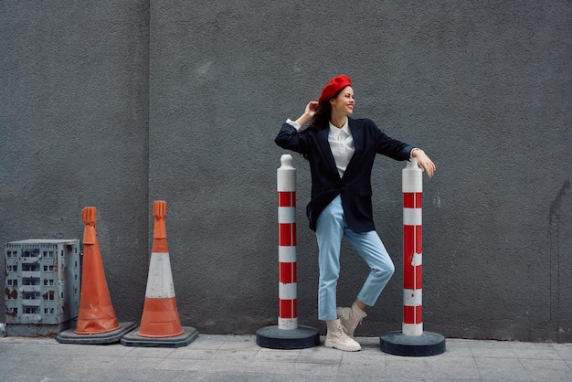 Mulher da moda em pé encostado em uma rua de parede contra um fundo da estrada da cidade trabalha turista em roupas elegantes com lábios vermelhos e boina vermelha viagem cor cinematográfica estilo retrô vintage