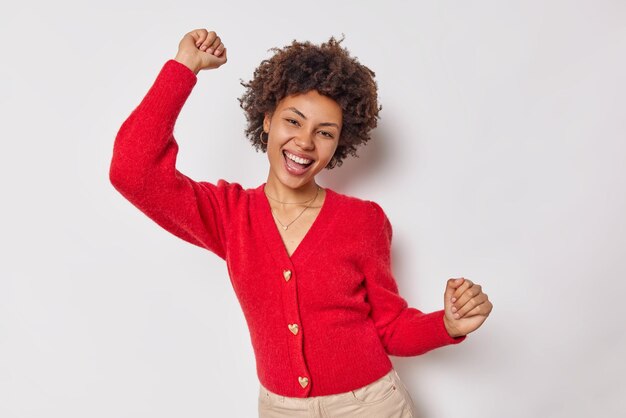 Foto mulher dançando dentro de casa contra o branco sacudindo os braços, rindo alegremente, se divertindo, usa um macacão vermelho casual que se move muito feliz com o ritmo da música