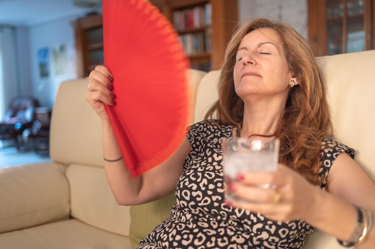 Mulher dando-se ar com um ventilador e um copo de água com gelo para se refrescar no verão