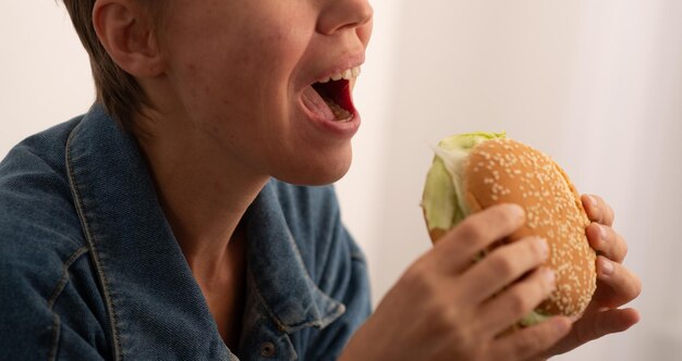 Foto mulher de 40 anos a comer um grande hambúrguer em close-up.