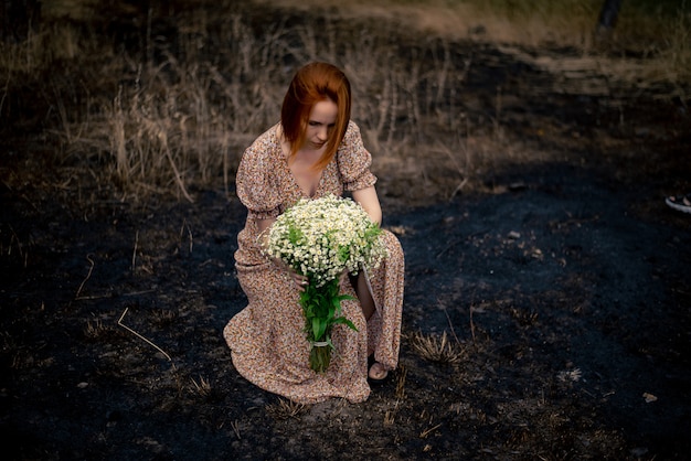 Mulher de 40 anos com um buquê de flores silvestres na terra arrasada, conceito de esgotamento psicológico