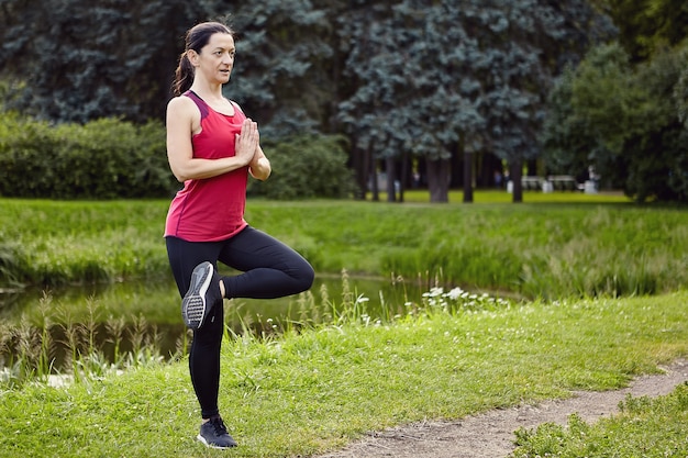 Mulher de 40 anos faz exercícios físicos ao ar livre em roupas esportivas.