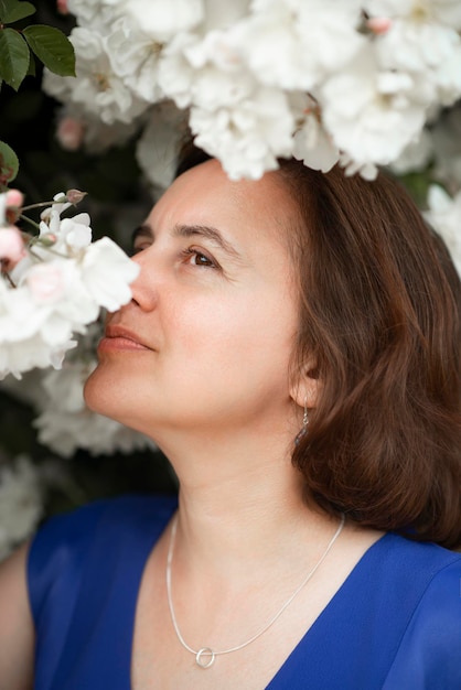 Mulher de 48 anos em um vestido azul perto de uma rosa branca florescendo