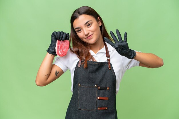 Mulher de açougueiro vestindo um avental e servindo carne fresca isolada em fundo croma verde feliz e contando quatro com os dedos