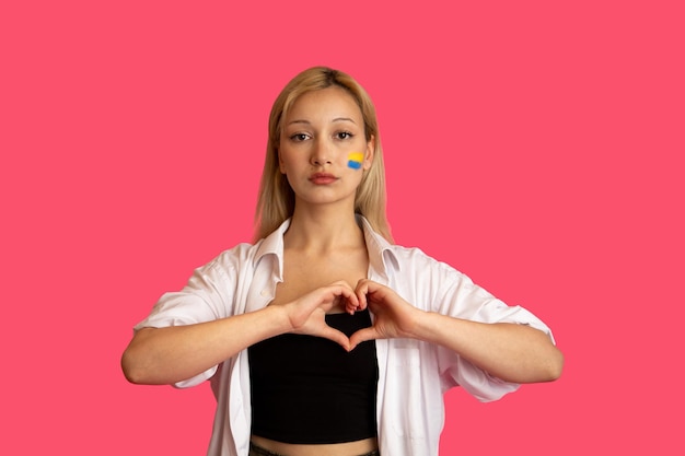 Foto mulher de aparência de modelo com a bandeira da ucrânia no rosto se posiciona em um fundo rosa