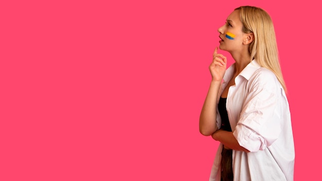Mulher de aparência de modelo com a bandeira da Ucrânia no rosto se posiciona em um fundo rosa