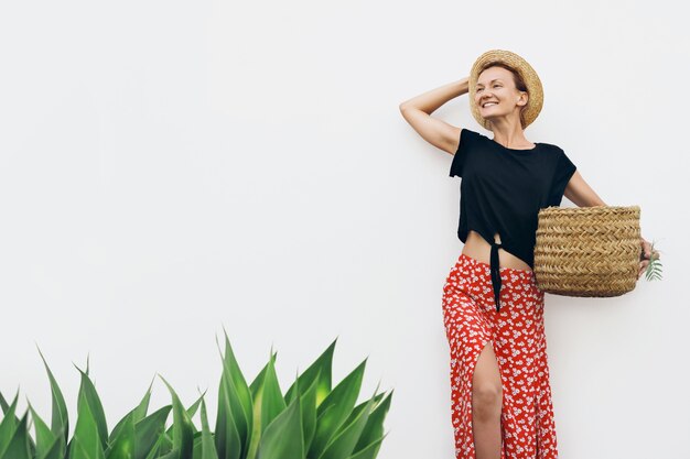 Foto mulher de aparência rústica segurando uma cesta contra uma parede branca com plantas verdes fotografia estilo minimalista