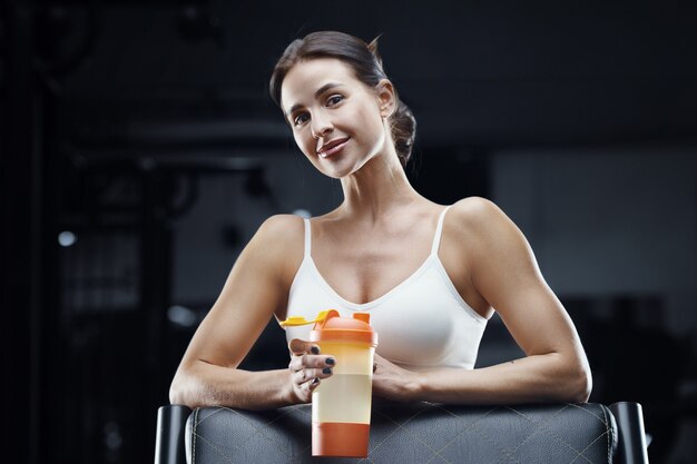 Mulher de aptidão atlética bebendo água do agitador de laranja no treino no ginásio. menina bonita caucasiana atlética. conceito de fitness e esporte.
