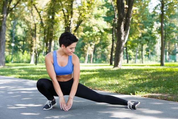 Mulher de aptidão esticando as pernas antes de correr ao ar livre. Jovem magro faz exercícios de aeróbica no parque, copie o espaço