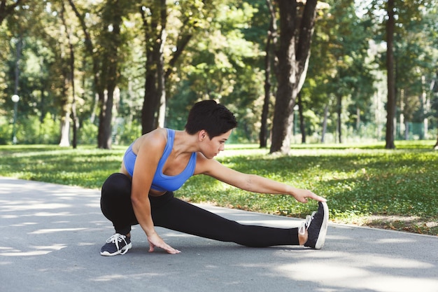 Mulher de aptidão esticando as pernas antes de correr ao ar livre. Jovem magro faz exercícios de aeróbica no parque, copie o espaço