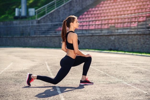 Mulher de aptidão fazendo rotina de aquecimento no estádio antes do treino, esticando os músculos do corpo