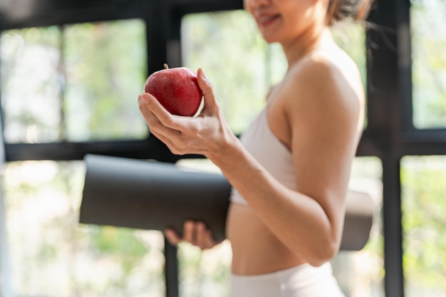 Mulher de aptidão segurando tapete de ioga com comida vegana limpa Fresh Apple Heathy antes de malhar no estúdio de ioga