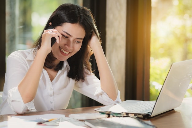 Mulher de ásia que usa o smartphone, computador pessoal que trabalha com feliz.