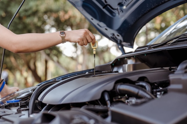 Mulher de autoatendimento usa vareta de nível de óleo para verificar o nível de óleo do motor, manutenção e reparos