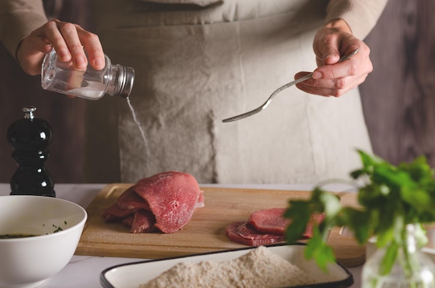 Mulher de avental bege coloca sal na carne O processo de preparação de milanesas argentinas