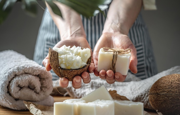 Mulher de avental segura um pedaço de sabão de coco artesanal branco e tigela com manteiga de coco fresca nas mãos conceito de fazer e usar sabão natural e cosméticos ecológicos um interessante passatempo criativo